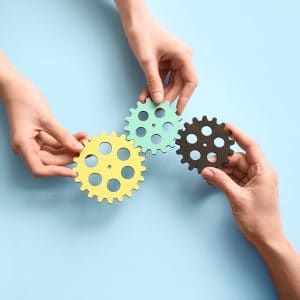 Two pairs of hands holding cogs together so that they connect